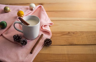 Sonbahar kış konsepti için sıcak içecek. Beyaz bardakta tarçın ve kozalaklı sıcak süt, Noel süslemeleri, ahşap arka planda süveter..