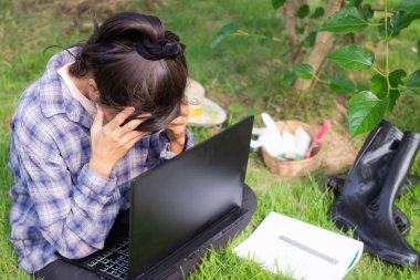 Stresli çiftçi ve baş ağrısı konsepti. Çiftçi dizüstü bilgisayar ve çim tarlasında kitap ile oturuyor. Bahçıvanlık eksikliğinden dolayı stres altında.. 