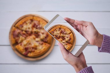 Süveter fotoğraflı, akıllı telefonlu pizzacı kadın. Fast food ve teknoloji konsepti.