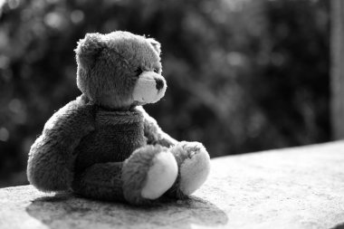 Kırık kalp konsepti. Oyuncak ayının beton duvarda oturan üzgün suratının siyah ve beyaz görüntüsü. Yalnızlık, yalnızlık, terk edilmiş çocuk, kavramsal.