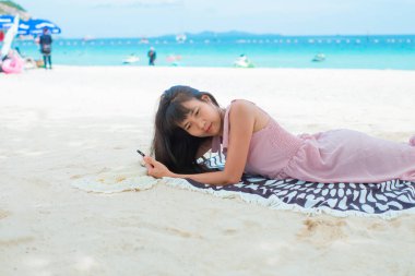 Asyalı kadınlar pembe elbiseleriyle deniz sahilinde dinleniyor. Yaz tatilinde kumsalda mavi gökyüzü ve deniz ile mutlu. Projeniz için yaz mevsiminde turizm ve seyahat metinlerini düzenliyor.