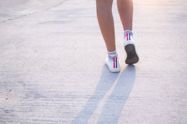 Otantik ince ve ten rengi bacakları olan beyaz spor ayakkabılı bir kadın egzersiz yapmak için yolda yürüyor. Yalnızlık için kavramsal, kırılgan kadın yalnız ileri adım at, güçlü..