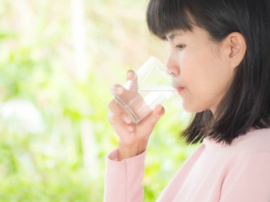 Asyalı kadın yeşil arka planda bulanık su içiyor. güzellik ve sağlık konsepti.