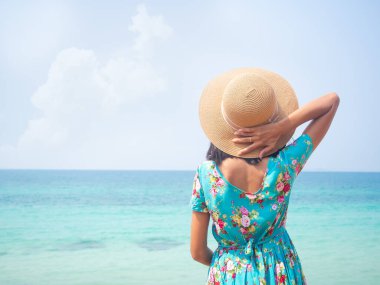Mavi deniz kıyısında duran şapkalı ve mavi elbiseli kadın. Güzel okyanus Tayland 'ı. Hakiki bronz tenli Asyalı kız. Hayat tarzı turistler tatillerde tropikal yaz tatiline çıkar..