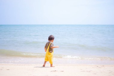 Şirin çocuk, kumsalda 17 ay boyunca bulanık mavi denizle beklemiş. O, yaz tatillerinde gülüyor ve eğleniyor. Tropikal konseptte mutlu aile tatili turistleri.