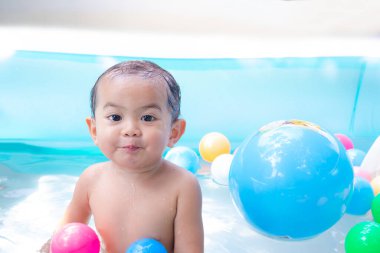 Plastik havuzunda su ve plastik top oyuncağıyla geçen 17 aylık tatlı bir çocuk. Çocuk suda oynarken eğlendi. Yaz tatilinde mutlu aile kavramı.