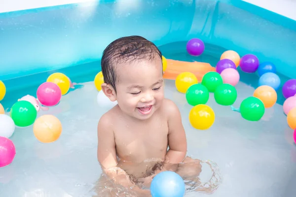 Cute little boy 17 month with water and plastic ball toy in plastic pool. child had fun playing in the water. happy family in summer hollidays concept.