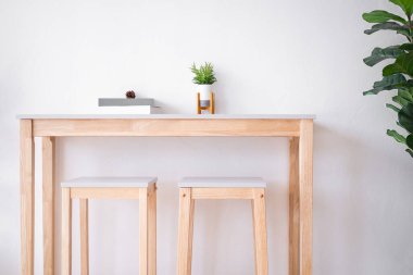 Tahta masadaki vazoda, sandalye ve duvar arkası beyaz çimento kaplı gerçekçi yapay ağaç. Lüks modern oturma odası. Ev konsepti..