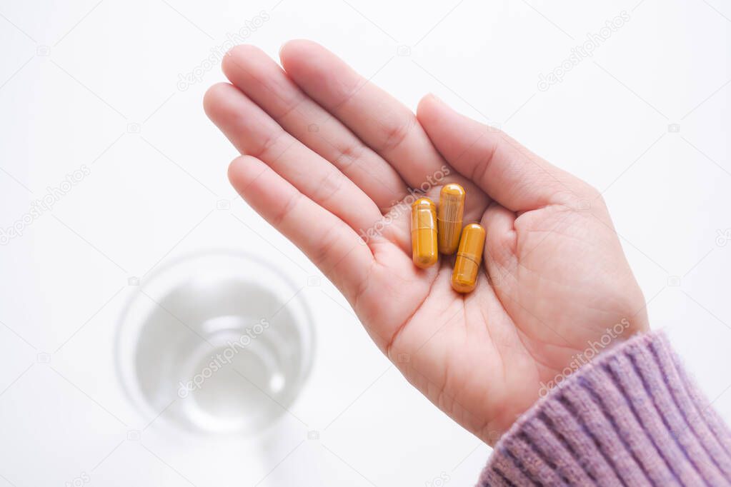 Turmeric capsule on palm up woman with sweater and blur water in glass on white background. thai organic herb. curcumin contains anti-oxidants helps to slow down aging and wrinkles.