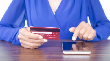 Personel kadın kredi kartı tutuyor ve ahşap masada dokunmatik ekranlı cep telefonu kullanıyor. İnternet üzerinden alışveriş yapmak ya da sosyal medyanın internet teknolojisi bankacılığına ödeme yapmak. iş ve finans kavramı.