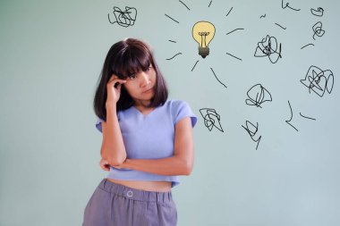 Yeşil duvar çimentosu üzerinde ampul ve sorun sembolleriyle duran genç bir kadın. Otantik ince yapılı, düzgün ve bronz tenli Asya Tayland dişisi. yaşam tarzı konsepti.