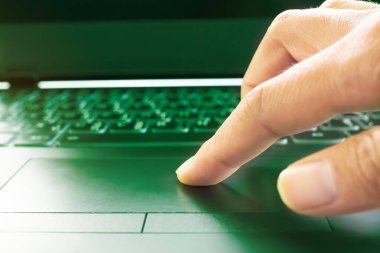 Parmak Touchpad klavye dizüstü bilgisayarında, yeşil ışık üzerinde. hacker, kimlik hırsızlığı, siber güvenlik, dijital teknoloji internet ağı çevrimiçi konsept.