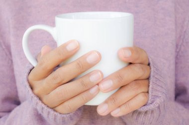 Süveteri olan bir kadın içmek için sıcak çay tutuyor. Evde tatilde yaşam tarzı. Kışın veya sonbahar mevsiminde yemek kahvaltısı. İyi sağlık konsepti için iç.