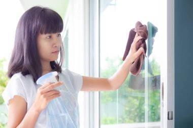 Tatillerde evin kapısını temizlemek için elinde bez ve cam temizleyici şişesi tutan Asyalı kadın portresi. Otantik siyah saç, ten teni ve ince yapılı kız Tayland. güzel konsept için ev dekorasyonu.