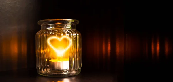 Glow pain shape heart in glass bottle with gold light candle on dark black background. for card poster couple love valentine day free space. alone sad brokent heart symbols concept.
