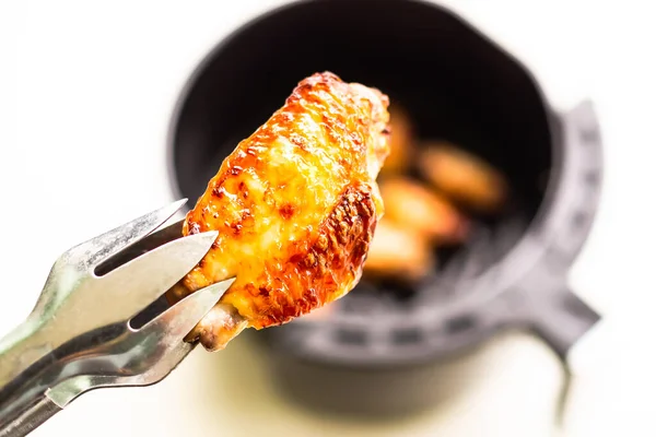 Beyaz masa arka planında Air Fryer 'da pişmiş tavuk kanatları ve maşayla bulanık tavuk kanatları. Düşük yağ kontrolü için yemek pişirmek. Sağlık konsepti için yiyecek.