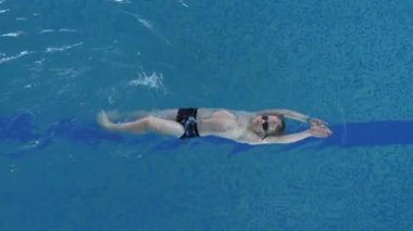 Beyaz çocuk havuzda sırt üstü yüzüyor. Yüzme Eğitimi ve Spor Etkinliği