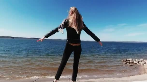 Το κορίτσι στην παραλία απλώνει τα χέρια της και τα μαλλιά της φτερουγίζουν στον άνεμο — Αρχείο Βίντεο