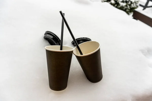 Two paper cups with coffee keep warm on a scarf in the snow, winter love tale