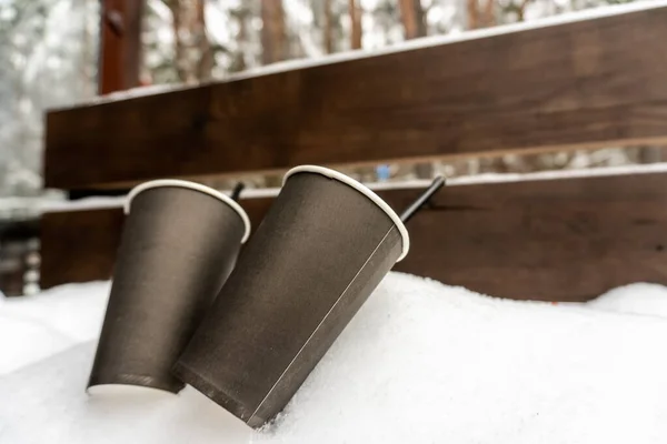 Two paper cups with coffee on a snow bench kissing each other in winter love