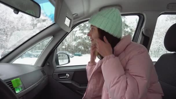 冬の帽子と冬のダウンジャケットで車の中で女の子は、トップミラーでは、彼女の髪をまっすぐに見えます。閉鎖 — ストック動画
