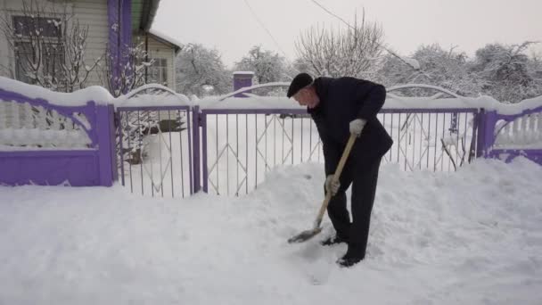 Um homem limpa a estrada da neve com uma pá, muita neve, inverno na aldeia — Vídeo de Stock