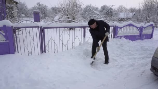 Ένας άνθρωπος καθαρίζει το δρόμο από το χιόνι με ένα φτυάρι, πολύ χιόνι, το χειμώνα στο χωριό — Αρχείο Βίντεο