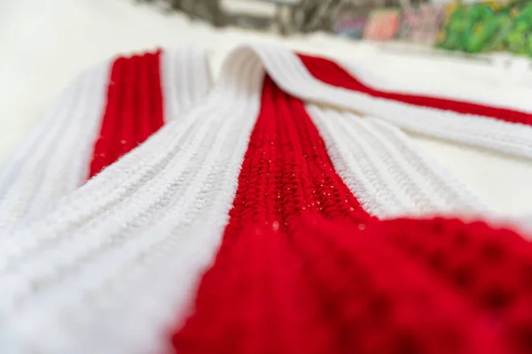 White-red-white knitted scarf on snow on the street in winter