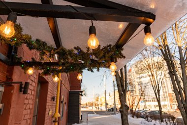 Kafe tepe örtüsü Edison ampulleriyle süslenmiş ve sıcak sarı bir ışıkla parlıyor.