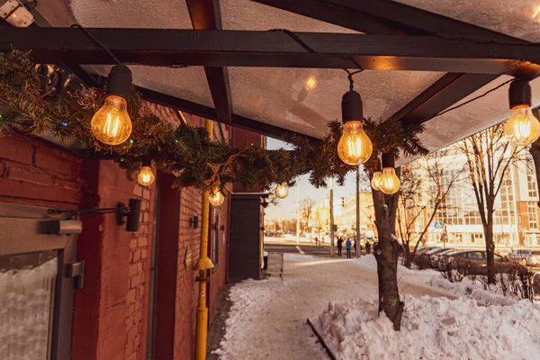 Cafe canopy is decorated with pine branches, Edison bulbs and shines with a warm yellow light — Stock Photo, Image