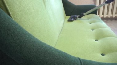 Elektrikli süpürgeyle toz kaldırıyorum. Evdeki yeşil kanepeyi temizlerken elektrikli süpürge kullanan bir adam.