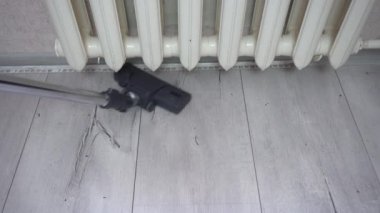 Elektrikli süpürge fırçası ısıtıcının yanındaki gri ahşap zemini temizler. Daire temizleme, gri parke süpürücü, döşeme kaplaması, hizmetçi haftalık temizliği.