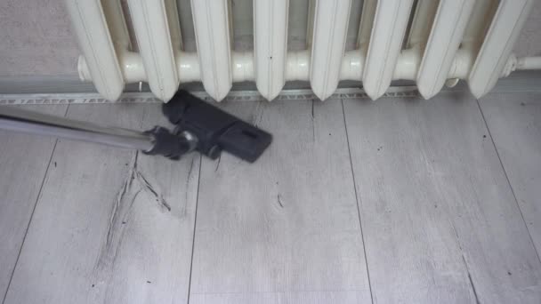 Sikat pembersih debu membersihkan lantai kayu abu-abu dekat radiator pemanas. Membersihkan apartemen, mengosongkan parket abu-abu dan lantai laminasi, pembersihan umum mingguan pembantu — Stok Video