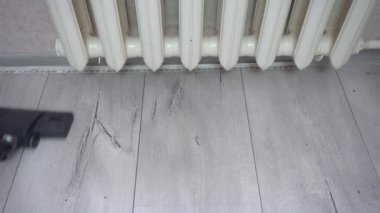 Elektrikli süpürge fırçası gri kaplamalı yüzeydeki tozu emer. Elektrikli süpürge fırçası ısıtıcının yanındaki gri ahşap zemini temizler. Hizmetçinin haftalık temizliği.