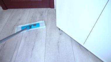 Mavi paspasla gri ahşap zemini temizliyorum. Kapının yakınını temizliyorum. Dolabın altını temizliyorum. Yakın plan.