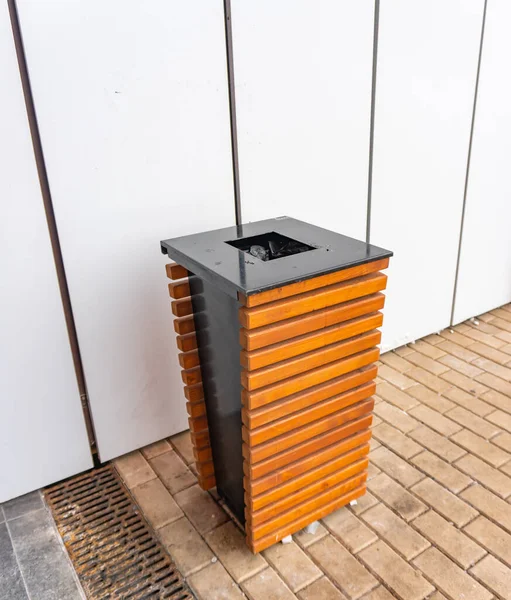 City trash can. Brown wooden trash can on a sidewalk near shopping center. Place for extinguishing cigarettes.