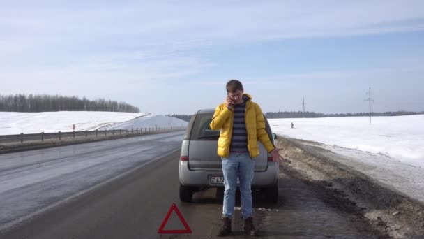 Ένας τύπος στέκεται κοντά σε ένα σπασμένο αυτοκίνητο και κάνει ένα ενεργό τηλεφώνημα — Αρχείο Βίντεο