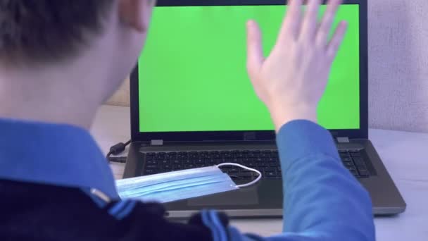 Un hombre saluda a sus colegas por vídeo llamando a un ordenador portátil y le recuerda que se ponga una máscara protectora, una pantalla de monitor verde — Vídeos de Stock