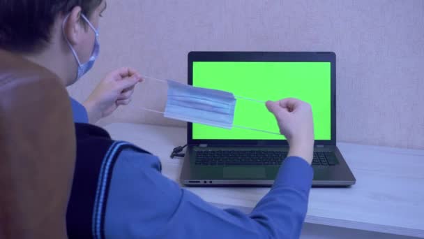 Chlap v lékařské masce si nasadí ochrannou masku na notebook s virtuálním partnerem, se kterým komunikuje přes video linku jako symbol ochrany proti viru, zelená obrazovka — Stock video