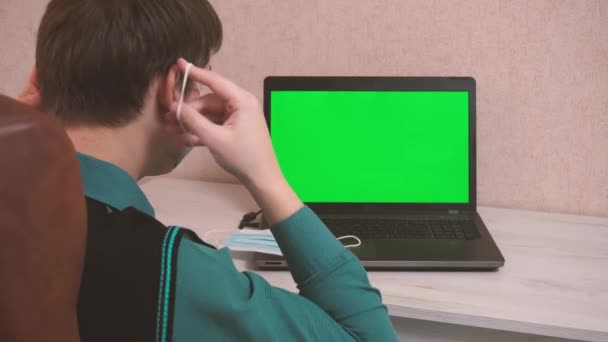 A man puts on a protective face mask himself and on the interlocutor by video call and starts typing on a laptop, epidemiological safety, remote work, green screen — Stock Video