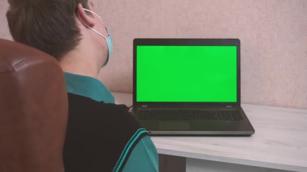 Un uomo che fa esercizi di riscaldamento mentre è seduto a un computer portatile tramite videochiamata in una maschera protettiva, cromokey — Video Stock