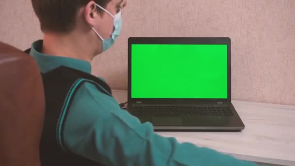 Egy férfi, aki bemelegítő gyakorlatokat végez, miközben egy laptopnál ül videohíváson keresztül, védőmaszkban, krómozva. — Stock videók