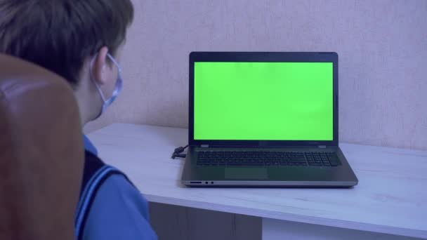 Un tipo con una máscara médica se pone una máscara protectora en un ordenador portátil con un interlocutor virtual con el que se comunica a través de un enlace de vídeo como símbolo de protección contra un virus, pantalla verde — Vídeo de stock