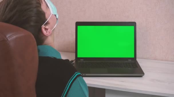 Un hombre haciendo ejercicios de calentamiento mientras está sentado en una computadora portátil a través de una videollamada en una mascarilla protectora, cromokey — Vídeos de Stock