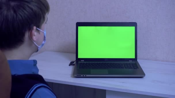Un tizio con una maschera protettiva ondeggia su una sedia durante una videoconferenza, comunicazione a distanza durante una pandemia — Video Stock