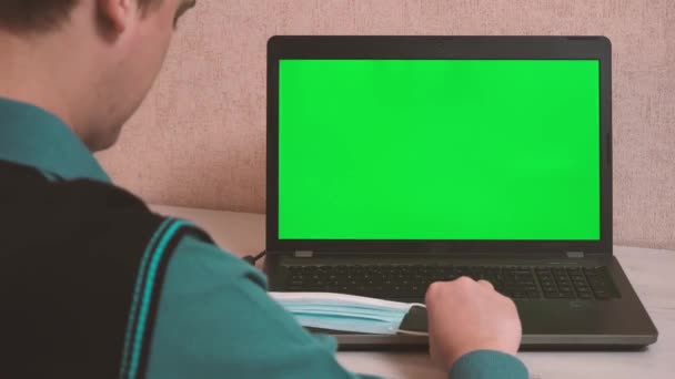 Muž nasadí ochrannou masku obličeje před zahájením práce na notebooku přes video komunikaci, chroma klíč na obrazovce notebooku — Stock video