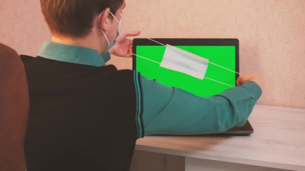 Ein Mann setzt sich selbst und dem Gesprächspartner per Videoanruf einen Mundschutz auf und beginnt auf einem Laptop zu tippen, epidemiologische Sicherheit, Fernarbeit, grüner Bildschirm — Stockvideo