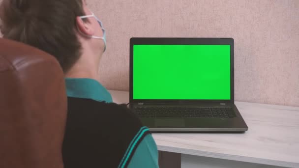 Un hombre haciendo ejercicios de calentamiento mientras está sentado en una computadora portátil a través de una videollamada en una mascarilla protectora, cromokey — Vídeos de Stock