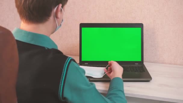 Egy férfi felvesz egy védő maszkot maga és a beszélgetőpartner videohívással, és elkezd gépelni egy laptopon, járványtani biztonság, távoli munka, zöld képernyő — Stock videók