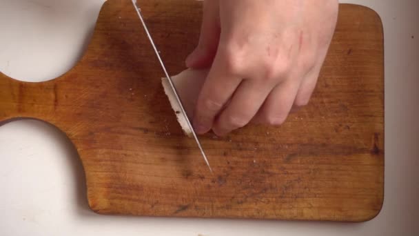 Рука розрізає великий шматок солоного салату на дрібні шматочки ножем на дерев'яній дошці — стокове відео